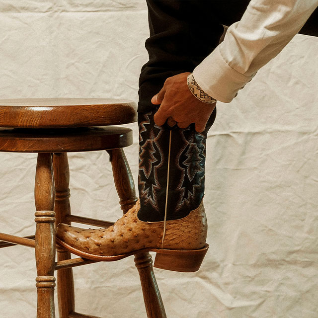 A man resting his foot on a stool and wearing Tony Lama Boots